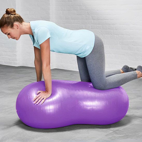 ballon de yoga cacahuète, une femme en position chien avec les genous et les mains sur le ballon 