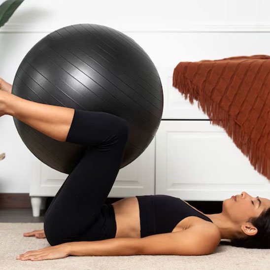 Ballon pilates, une femme couchée sur le dos et un ballon est entre les jambes qui sont pliés dans l'air